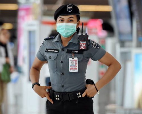 Bangkok, Thailand - February 18, 2020: A security guard looks-on as air travelers wearing masks walk through the departures hall of Suvarnabhumi Airport. Thailand has been assessed as a country at risk of Covid-19 outside of China.