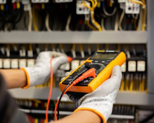 Electrician engineer uses a multimeter to test the electrical installation and power line current in an electrical system control cabinet.
