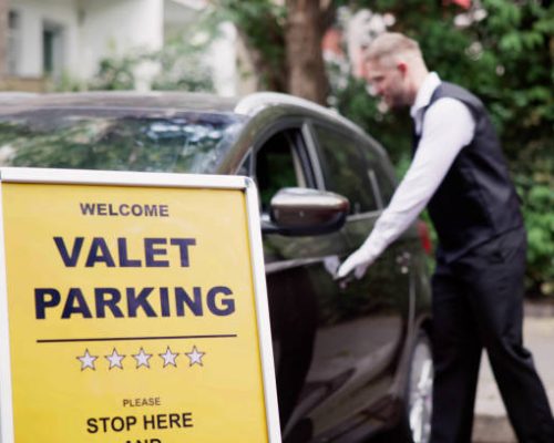 Man Giving Car Key To Male Valet Near Valet Parking Sign