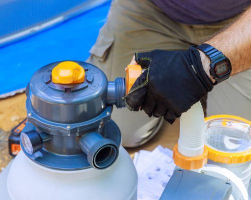 Swimming pool maintenance workers assemble sand filter system tank cleaning equipment