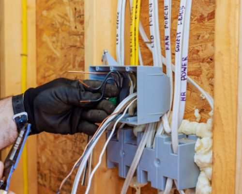 Electrician connects wires inside circuit box while renovating home, ensuring proper electrical setup